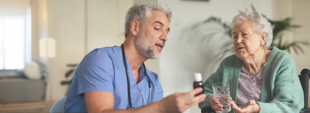 Caregiver showing medicine to an elderly woman holding a glass of water