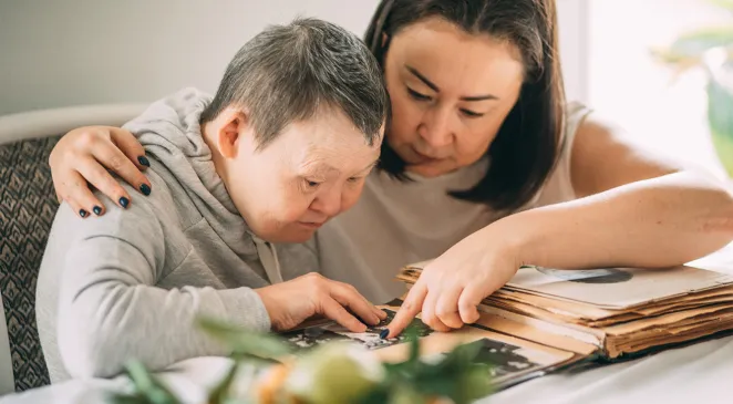 Elderly woman with Down syndrome looks at photos in an old album with a caregiver