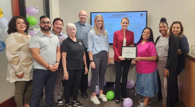 Home Assist Health employees smiling, while one employee holds a Caregiver of the Year award, in the office