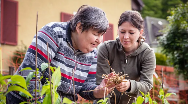A caregiver explains to a mentally handicapped woman how to mulch with straw