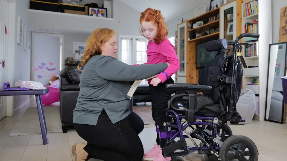 Mother helping her young daughter sit down in her wheelchair